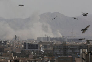 Pigeons flying over a smoke-filled Tehran skyline after a military attack.